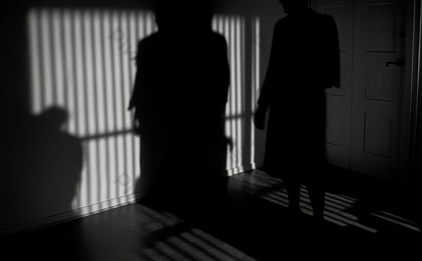 Một căn nhà có cửa mở hé, ánh sáng ban ngày chiếu rọi, hình bóng một người đang lén bước vào.