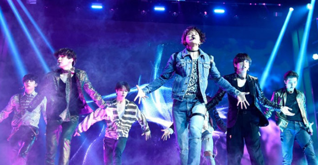 Một nhóm người đang hát trên sân khấu, khán giả bên dưới cười nói vui vẻ, không khí rộn ràng.