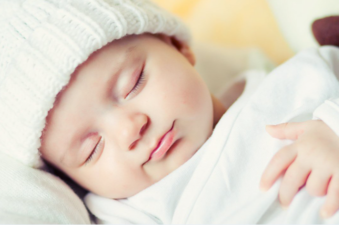 Một em bé sơ sinh đang ngủ ngoan trong tấm chăn trắng tinh khôi.