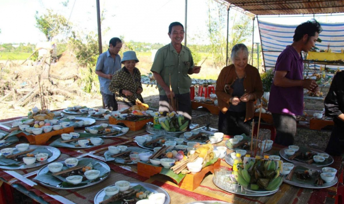 Một nhóm người trong sân đang chuẩn bị mâm gà, ánh nắng nhẹ chiếu lên khung cảnh quen thuộc.