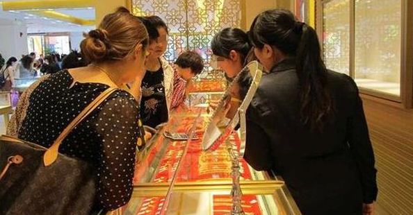 Một người đang chọn nhẫn vàng trong tủ kính, ánh đèn vàng ấm áp chiếu lên khuôn mặt đầy kỳ vọng.