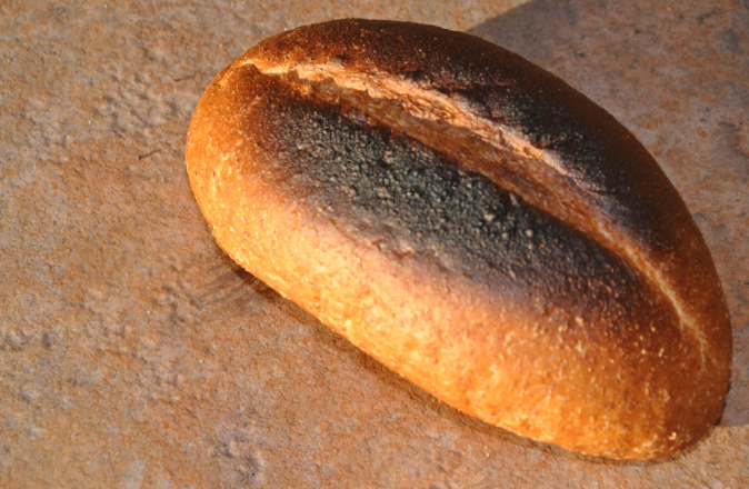 Ổ bánh mì cháy sém đặt trên bàn, ánh sáng mờ nhạt thể hiện cảm giác lo lắng và mất cân bằng.