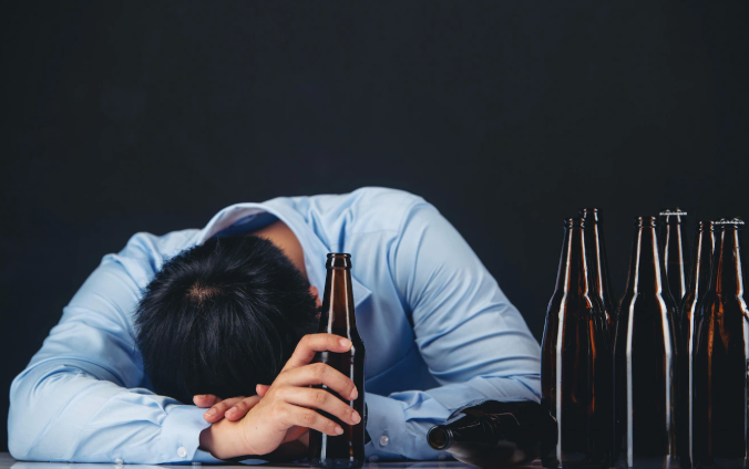 Hình người đàn ông ngả nghiêng trên bàn với chai rượu trống rỗng, ánh sáng vàng nhẹ để tăng cảm xúc.